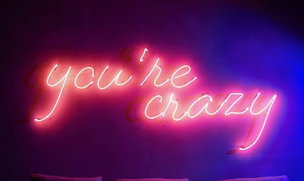 Neon sign reading 'you're crazy' in pink cursive lettering against a dark background with purple and blue lighting