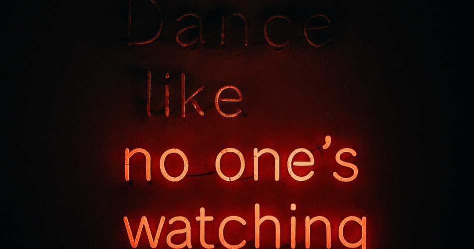 A neon sign on a dark wall that says “Dance like no one’s watching.” The words "dance like" are barely glowing. The rest glows softly in red, casting a faint light.