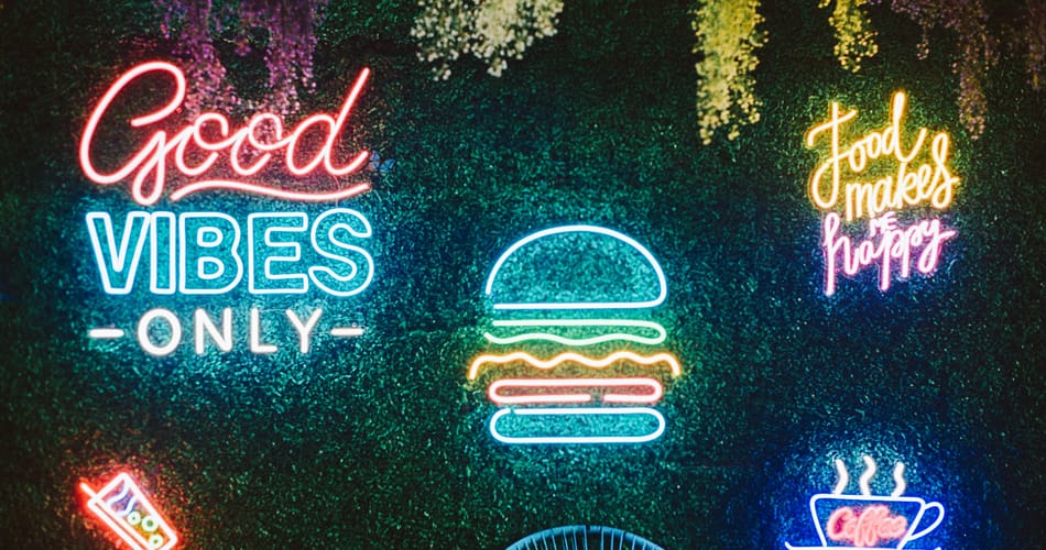 Vibrant neon wall art with positive messages including 'Good Vibes Only' and food-themed signs creating a cheerful, welcoming atmosphere