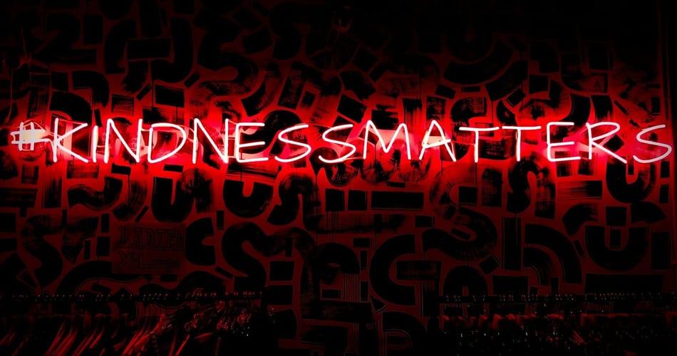 Red neon sign reading “Kindness Matters” against a dark background with layered graphic textures.